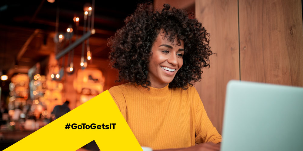 Donna che lavora da remoto in un bar protetta dai rischi per la sicurezza del lavoro a distanza grazie alle migliori pratiche dell'IT.