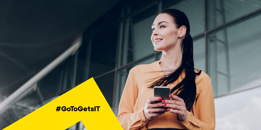 Woman holding mobile phone and smiling, representing the ability to leverage the end user’s mobile device camera to provide IT support via live visual engagement camera sharing